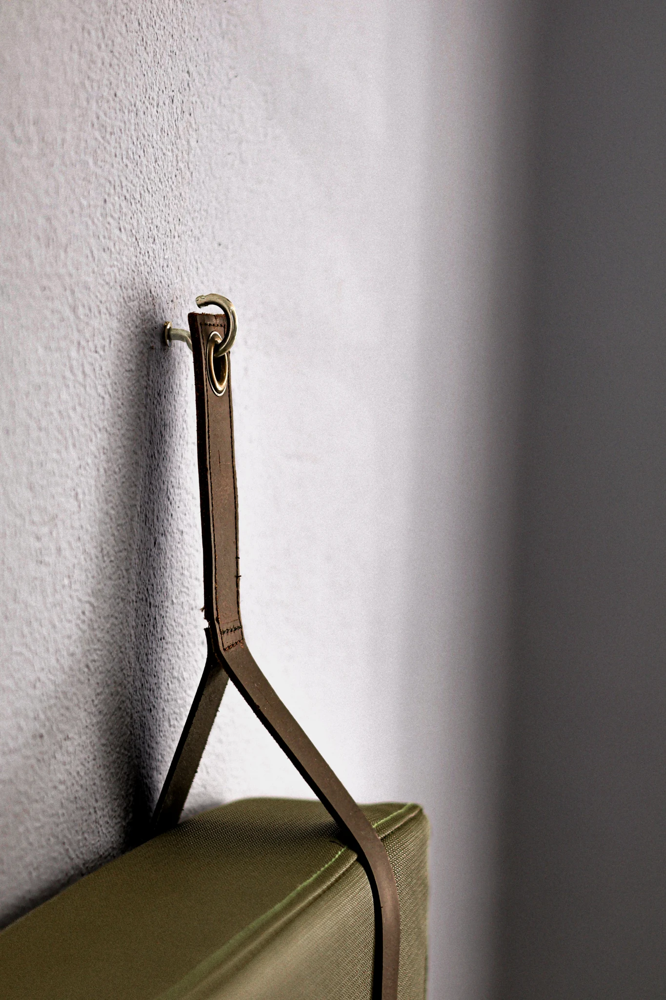A leather strap securing an olive upholstered bench backrest to the white wall.