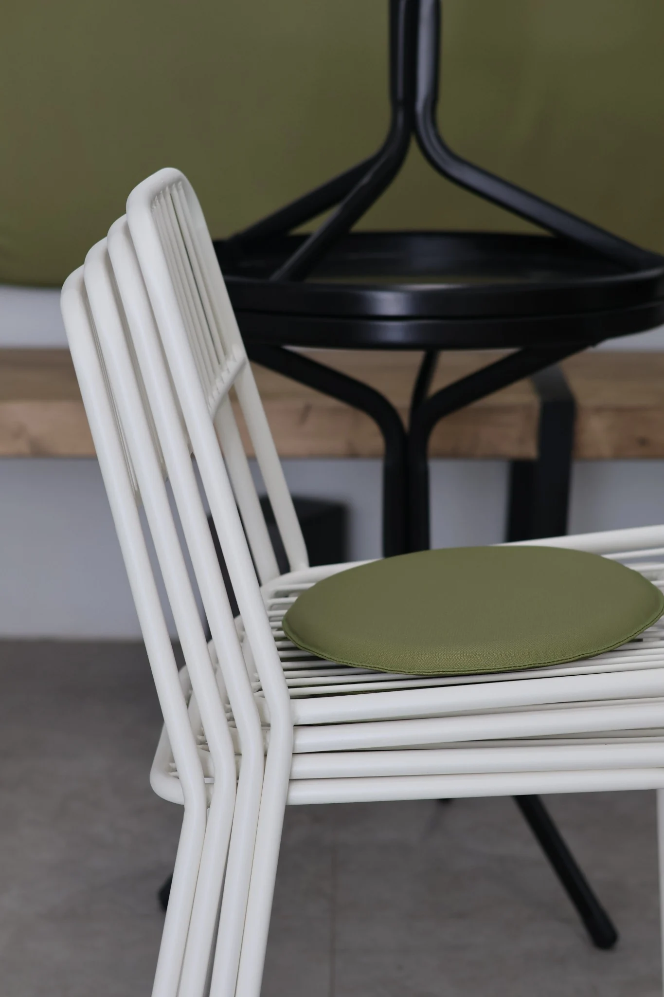 Close view of a white metal chair with an olive green seat cushion.