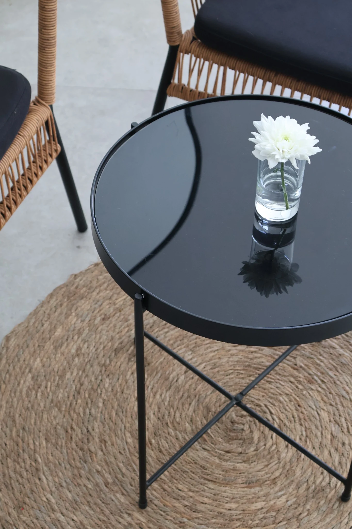 Small glass vase with a white flower on a glossy black café table.