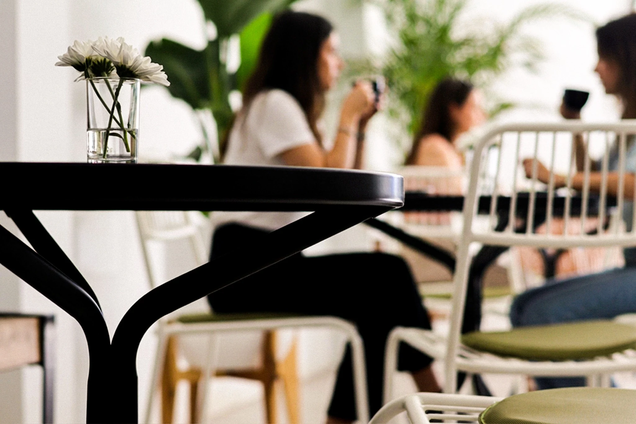 A café table and flower in focus, with people sharing coffee in the background.